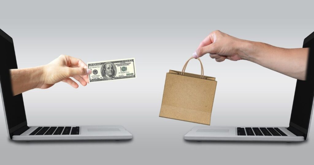 2台のパソコンから手が伸びて、お金と商品を交換するイメージ